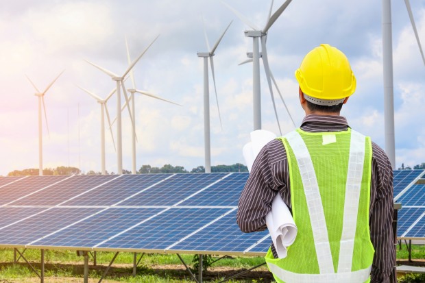 Young business man engineer with yellow helmet at solar panel and wind generators power plant construction site background