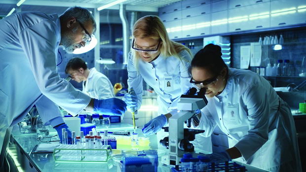 Team of Medical Research Scientists Work on a New Generation Disease Cure. They use Microscope, Test Tubes, Micropipette and Writing Down Analysis Results. Laboratory Looks Busy, Bright and Modern.